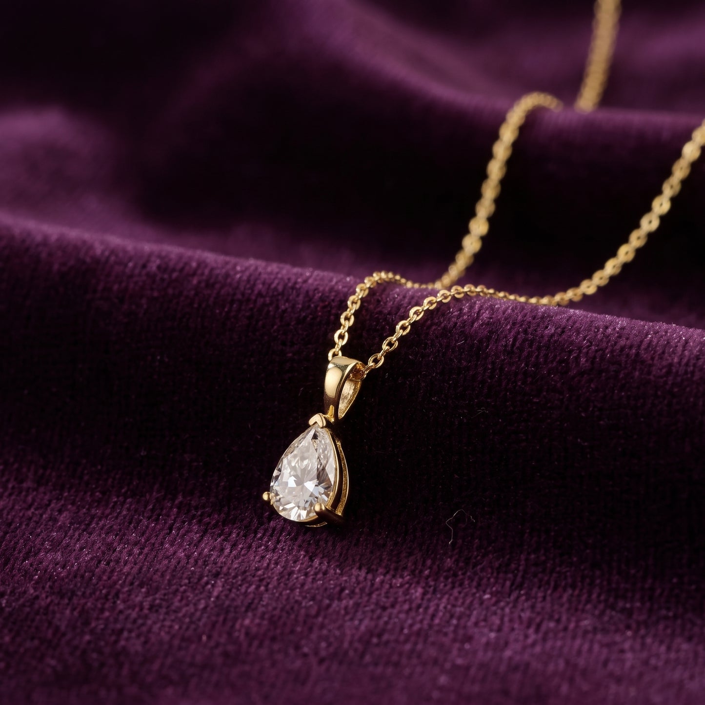 Gold necklace with a teardrop-shaped pendant on a purple fabric background