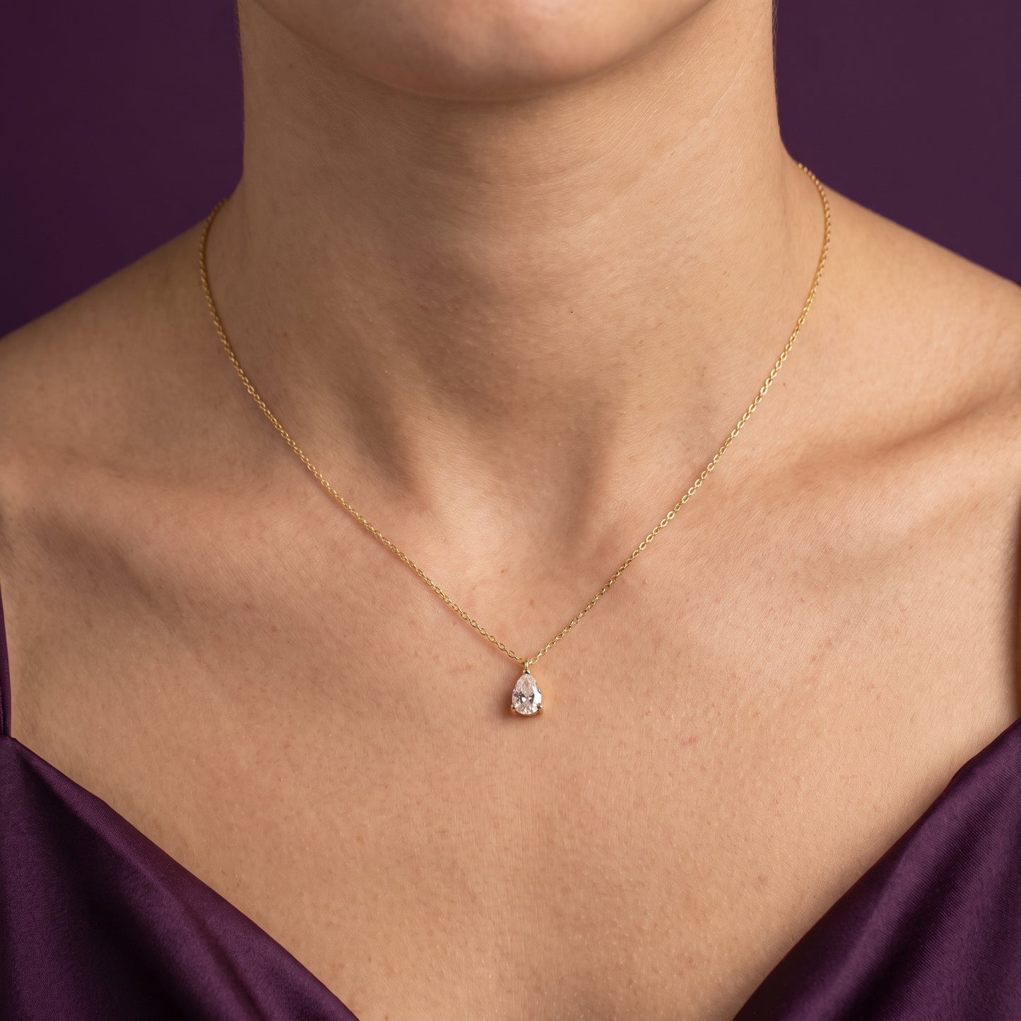 Gold necklace with a pendant on a person wearing a purple top against a dark background