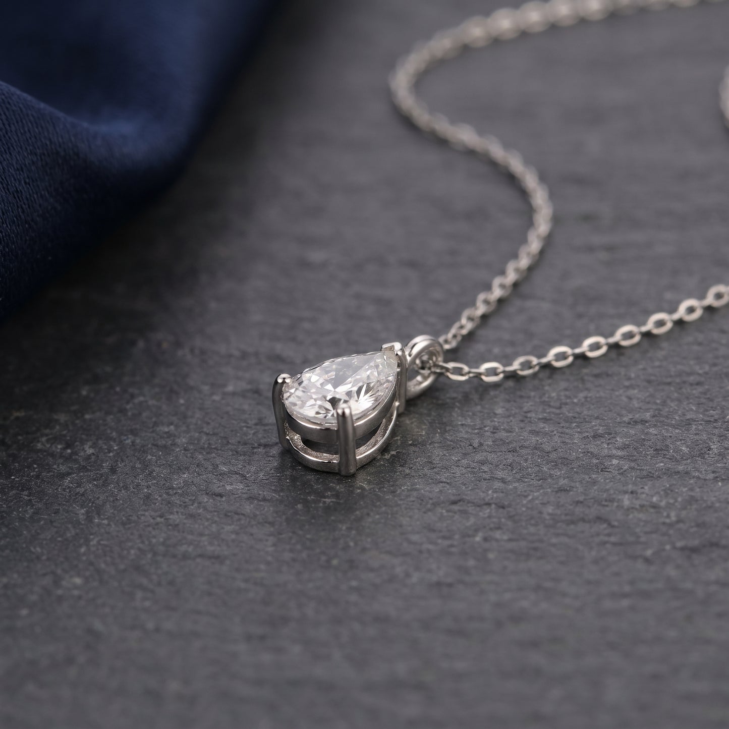 Silver necklace with a teardrop-shaped diamond pendant on a dark surface