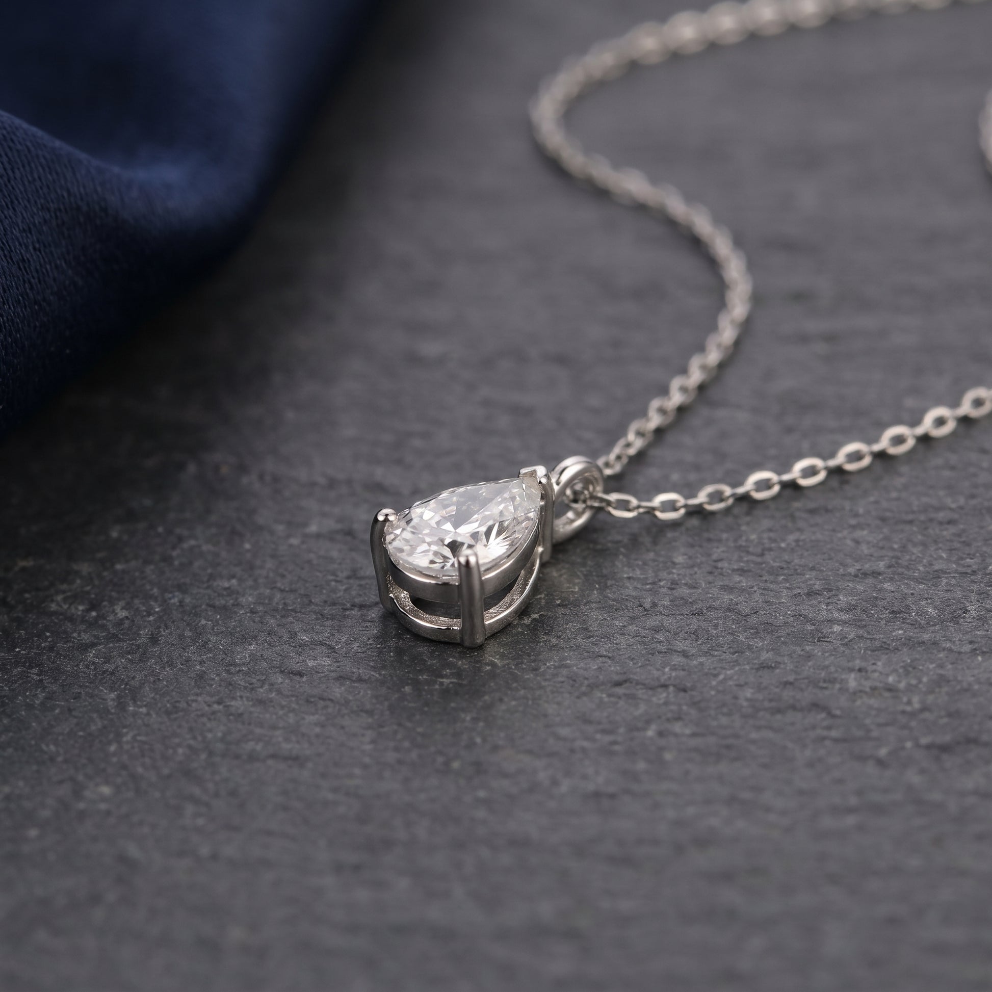 Silver necklace with a teardrop-shaped diamond pendant on a dark surface